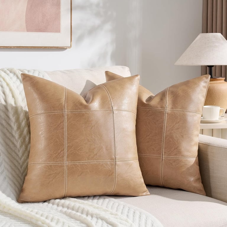 Two tan faux leather decorative throw pillows with a modern grid pattern on a white living room sofa.