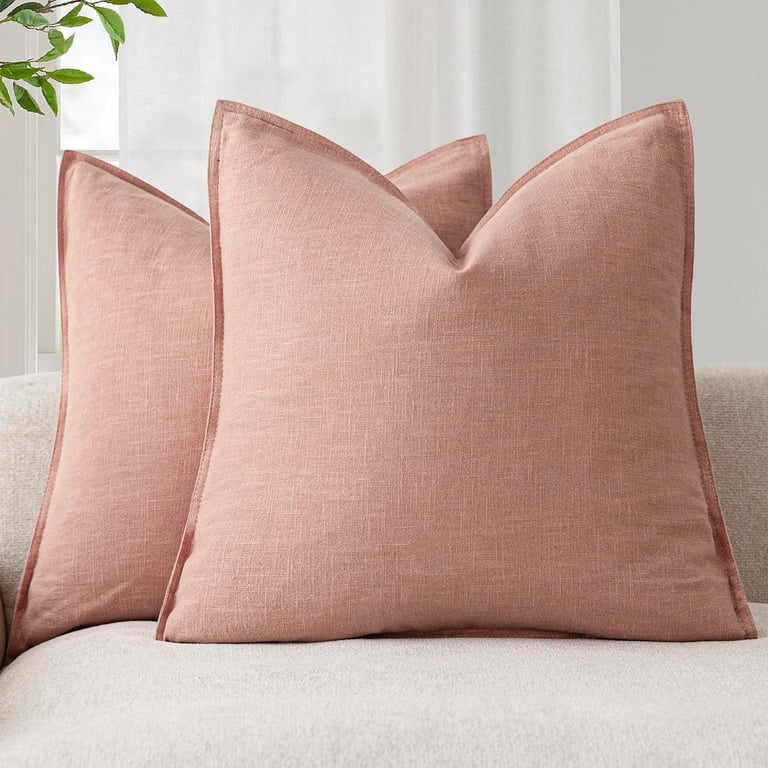 Set of dusty rose linen throw pillows with flanged edges arranged on a light-colored sofa.