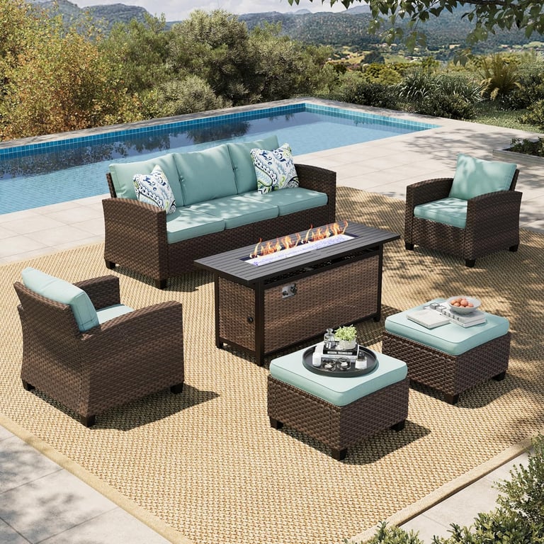 Wicker patio furniture set with turquoise cushions and a gas fire pit table next to a swimming pool.