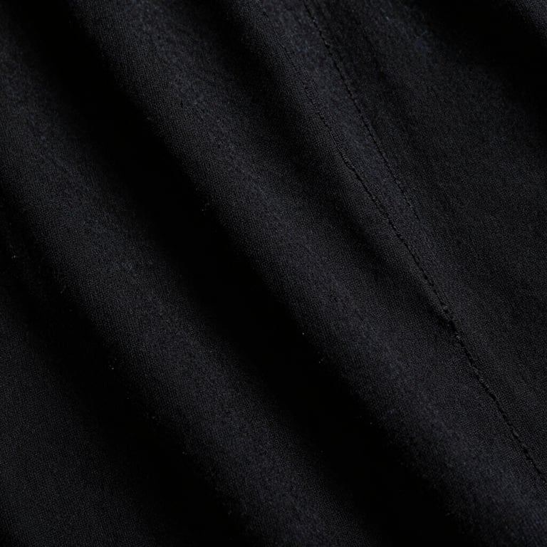 Low-key close-up of heavy black cotton fabric texture, showing the coarse weave and structural seams under dramatic side-lighting, high contrast, 35mm film