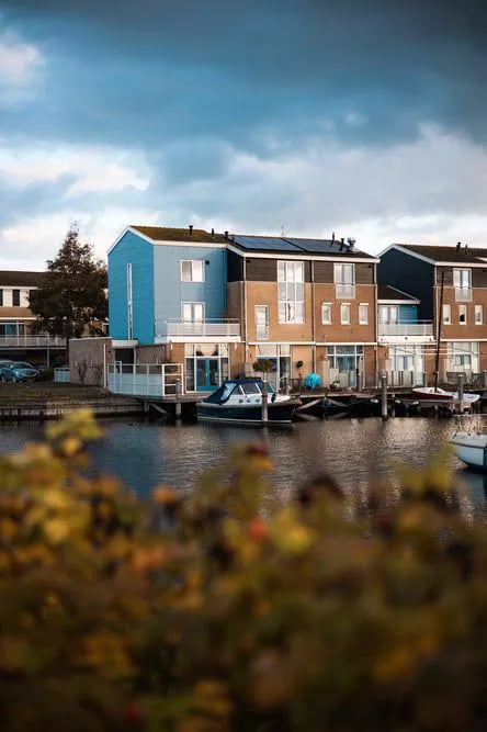 Moderne Häuser am Wasser mit privaten Bootsanlegestellen und Solaranlagen unter einem bewölkten blauen Himmel.