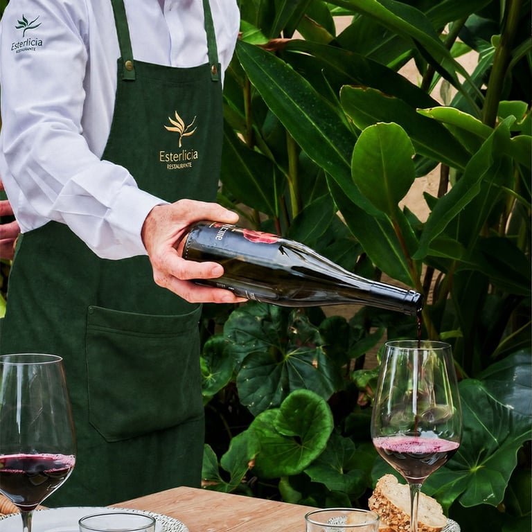 Mozo sirviendo vino vistiendo delantal e identidad bordada de la marca