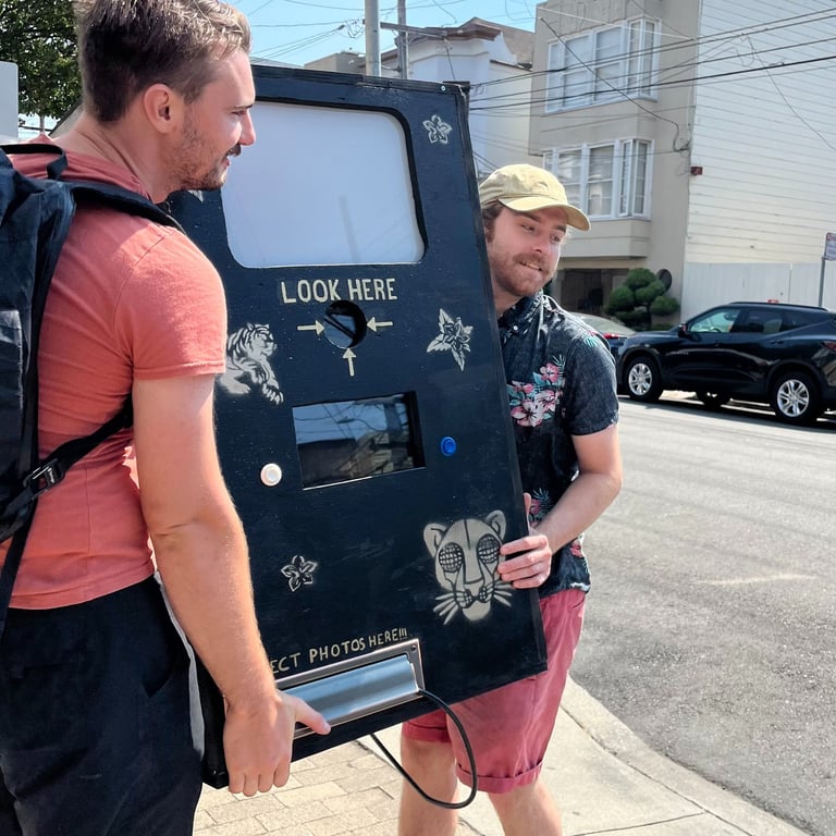 two men carrying a prototype photobooth made from wood