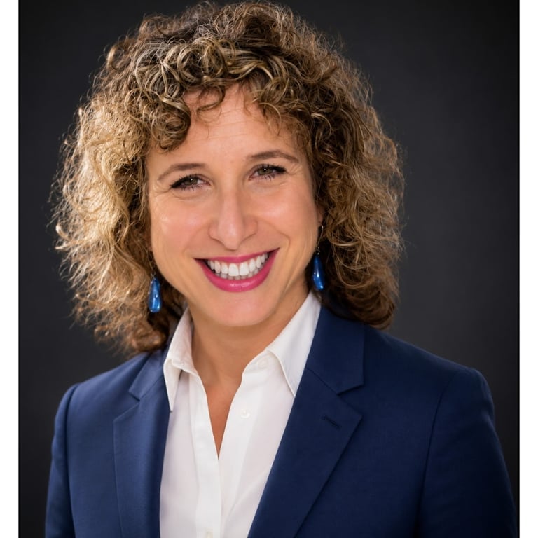 Professional headshot of a smiling woman with curly hair wearing a blue blazer and white shirt.