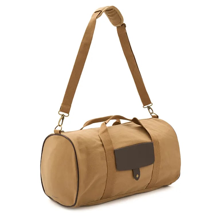 Durable tan canvas duffle bag with a brown leather patch and adjustable shoulder strap for travel.