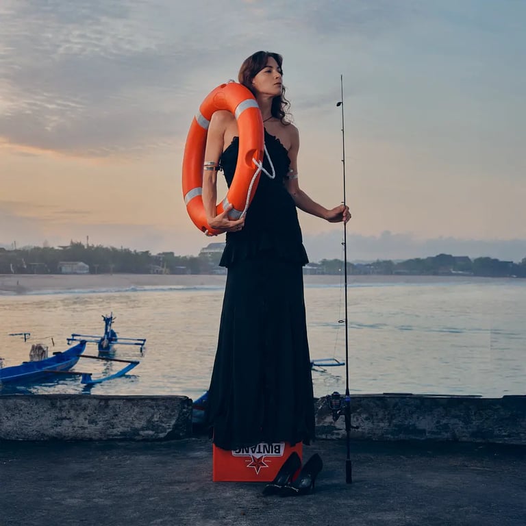 Model in black maxi dress standing on Bintang crates, holding fish rope and life buoy for Harbor Muse editorial.