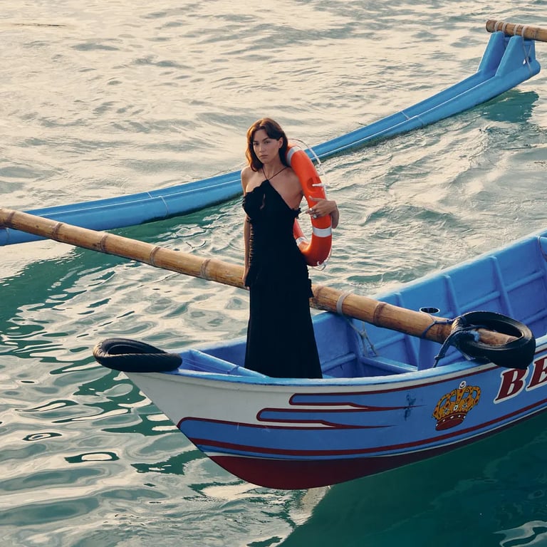 Model in black dress holding life buoy on a boat under soft sunrise for Harbor Muse editorial.