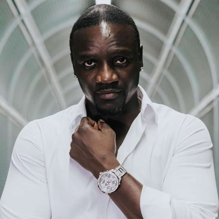 Singer Akon wearing a white shirt and luxury watch while posing in a tunnel.