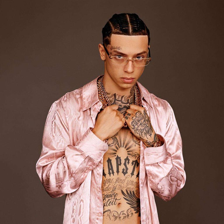Portrait of Central Cee wearing a pink silk shirt, gold chains, and glasses with visible tattoos.