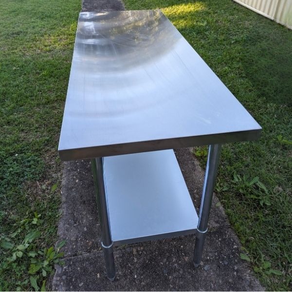 Table Hire: Long stainless steel workbench with undershelf, ideal for outdoor events.