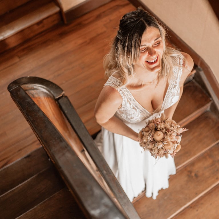 une mariée en robe de mariée qui rigole en haut des escaliers