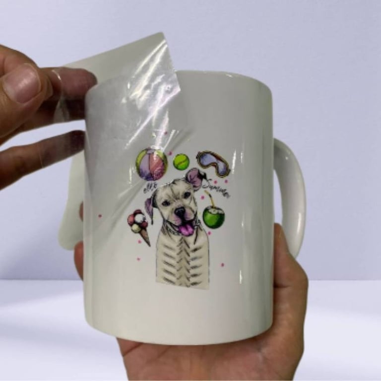 UV DTF sticker being applied to a white ceramic mug with a dog design.
