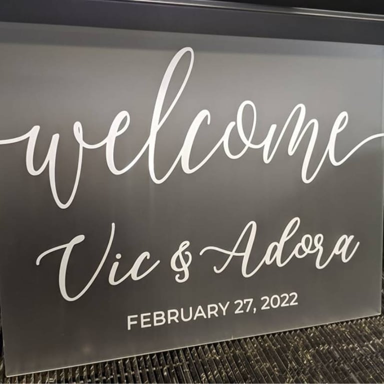 Gray acrylic welcome sign with 'Vic & Adora, February 27, 2022' in white script, ready for a wedding