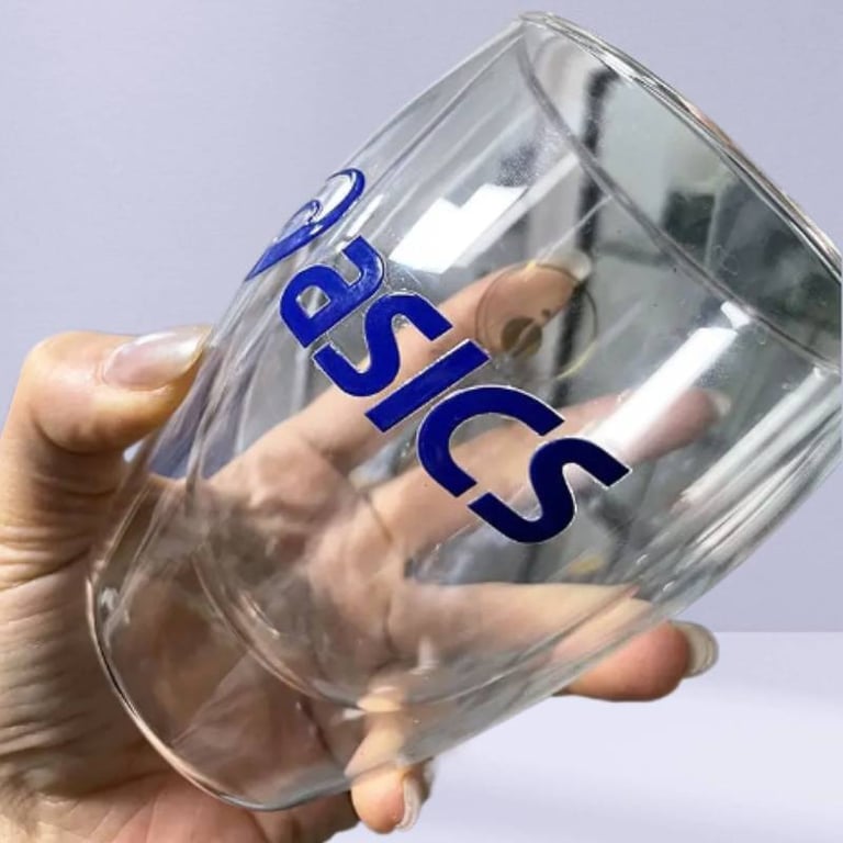 Hand holding a clear glass mug with a UV DTF printed 'Basics' sticker.