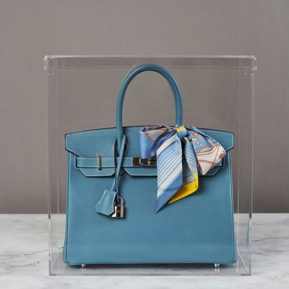 Blue luxury bag in a sleek acrylic display case.