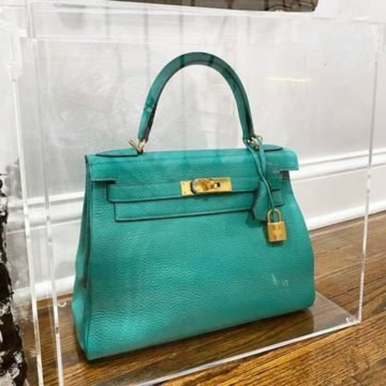 Teal designer handbag showcased in clear acrylic box.
