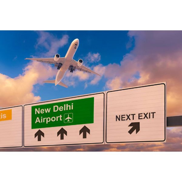 a plane flying over a highway sign new Delhi airport with a plane in the background