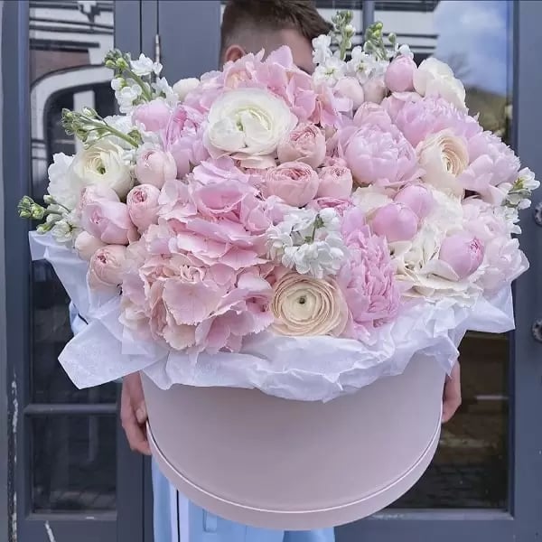 a man holding a large pink flower in a hat box