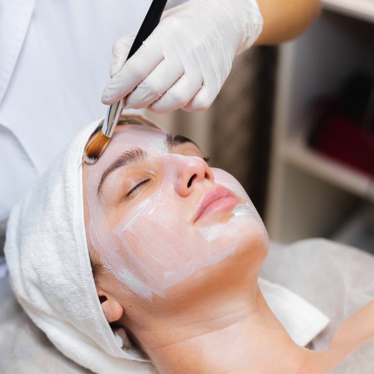 Beautician with a brush applies a white moisturizing mask to the face of a young girl client in a sp