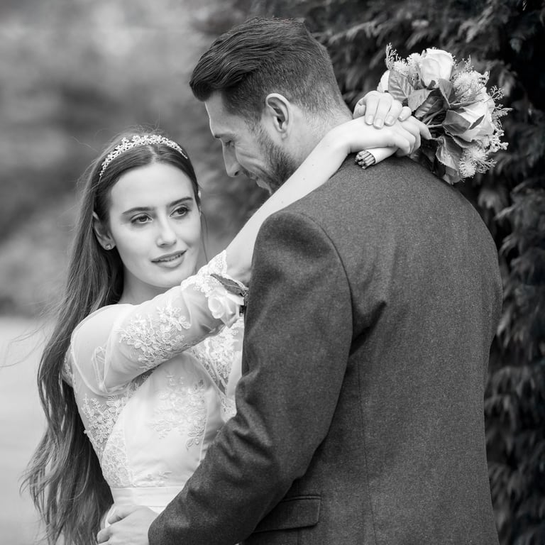 black and white editorial photo of bride and groom holding each other, groom admiring bride, bride looking into distance