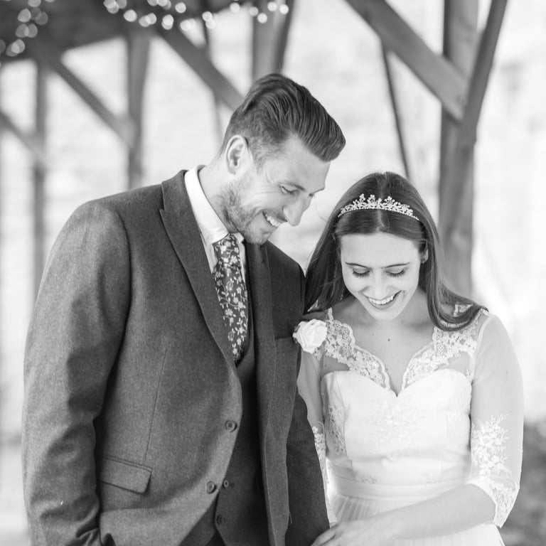 black and white photo of bride and groom holding hands walking and with big smiles on faces