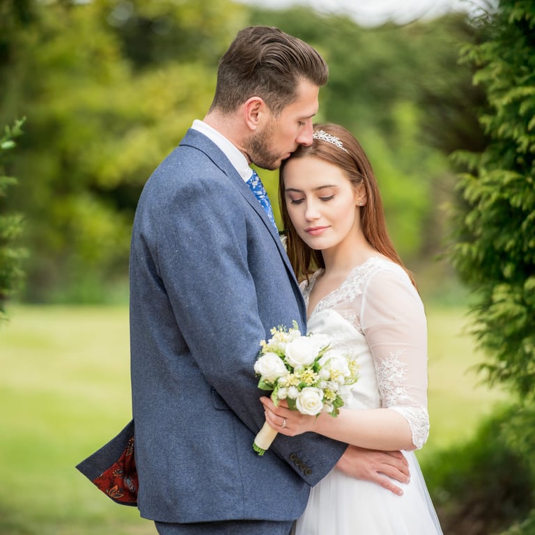 romantic photo of bride and groom holding each other, groom kissing bride, bride eyes closes with a little smile
