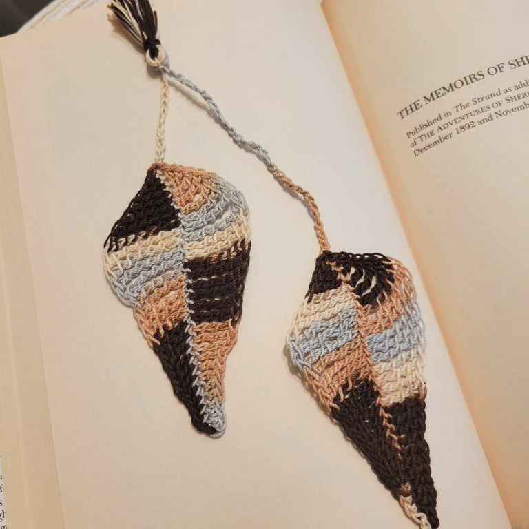 Handmade crochet leaf bookmark in neutral brown and beige tones resting inside an open book.