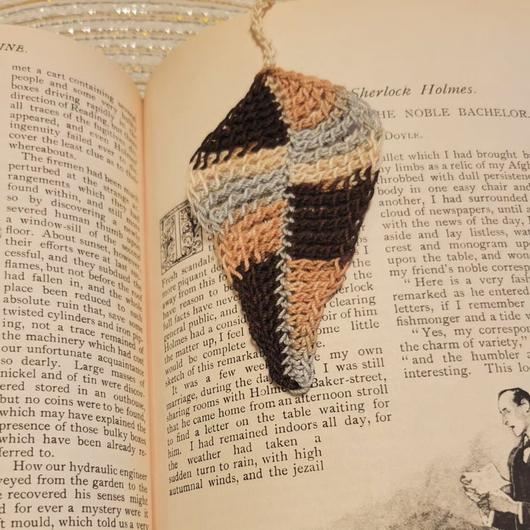 Handmade brown and tan crochet leaf bookmark resting on pages of a Sherlock Holmes book.