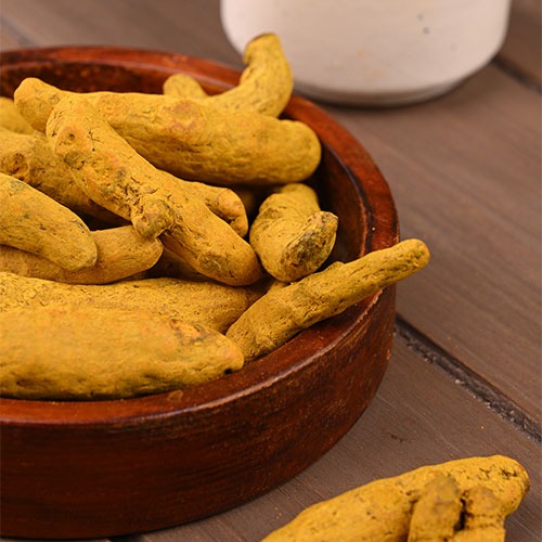 Dried whole turmeric roots in a small wooden bowl on a rustic table.