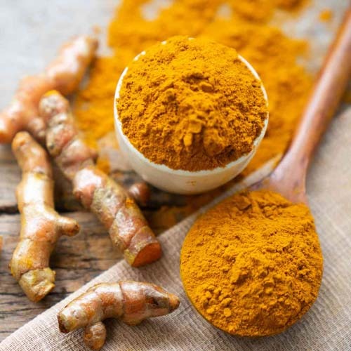Fresh organic turmeric powder in a small bowl and wooden spoon on a rustic surface.