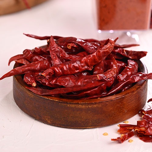 A wooden bowl filled with whole dried red chili peppers for spicy cooking.