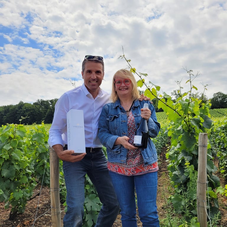 Patrice et Nathalie dans les vignes présentant la bouteille et l'étui du Champagne La Bulle du Bassi