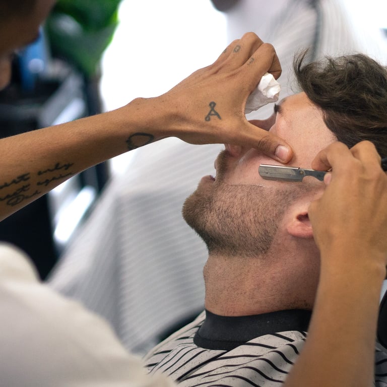 man receiving a shave with a cut throat razor by a barber while sitting in a chain in a barbershop