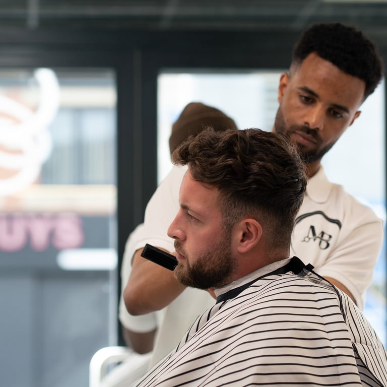 Side View of a customer having his hair cut by a barber while sat in a striped gown