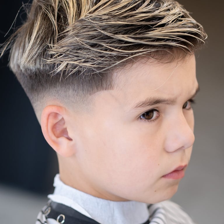side view of kid with freshly cut hair and  highlights sitting in a barber chair with a cape on.
