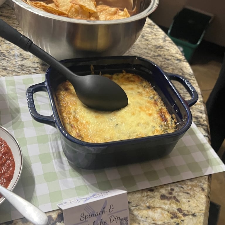 Square dish of spinach and artichoke dip with a metal bowl of tortilla chips sitting on a counter
