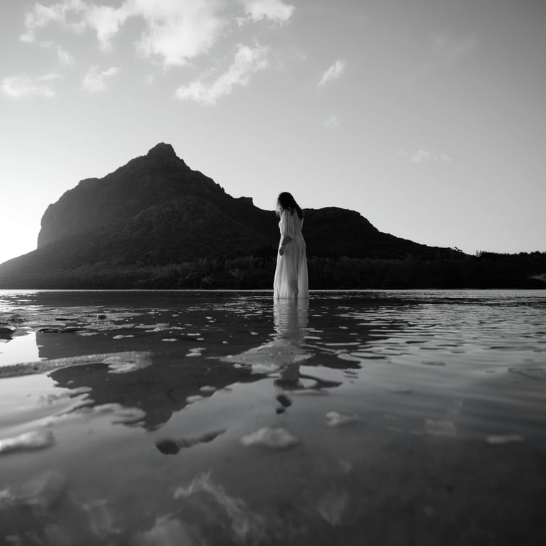 Woman standing in shallow water at sunrise near Le Morne Mountain in Mauritius, captured in dramatic black and white photo