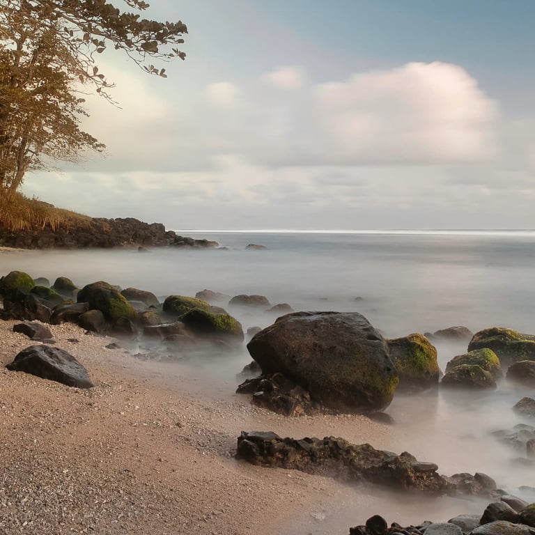 Peaceful morning on a secluded Souillac beach in Mauritius, with moss-covered rocks and soft waves gently washing ashore