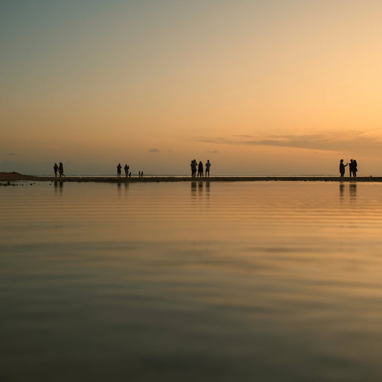 Silhouettes of people walking along the shoreline at sunset in La Prairie, Mauritius, with calm waters reflecting golden hues