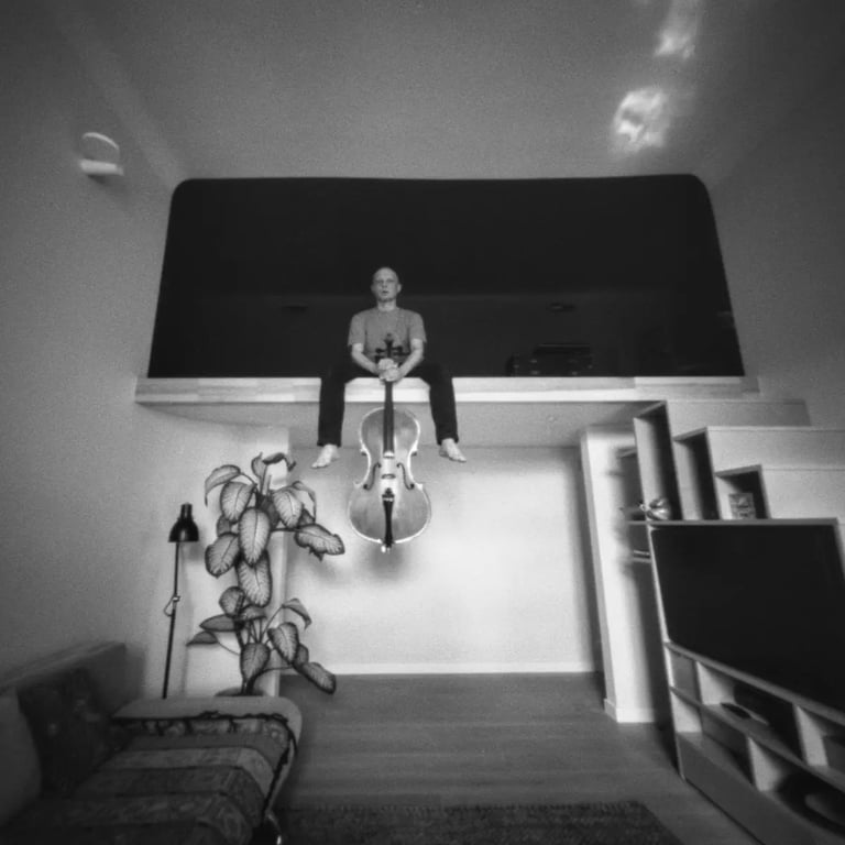A man sitting on a bed in a room, holding cello