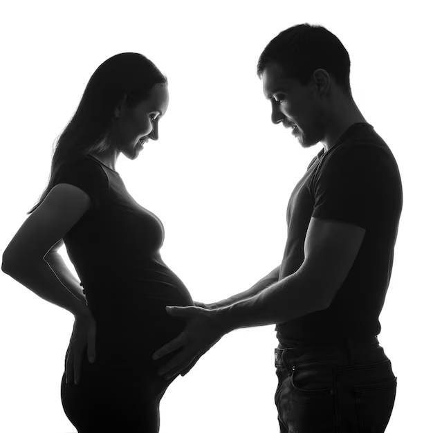 Silhouette of a smiling man holding his pregnant wife's belly during a maternity photo shoot.