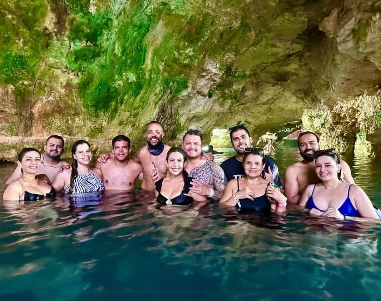 Grupo de turistas nadando em um cenote paradisíaco em Punta Cana, cercado por formações rochosas 