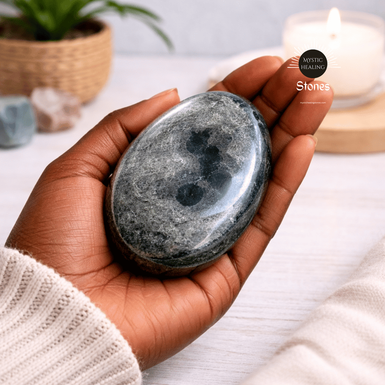 A hand holding a polished smoky obsidian crystal palm stone for healing.