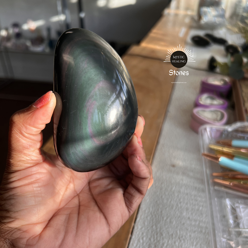 Polished velvet obsidian palm stone with iridescent pink and green sheen held in hand.