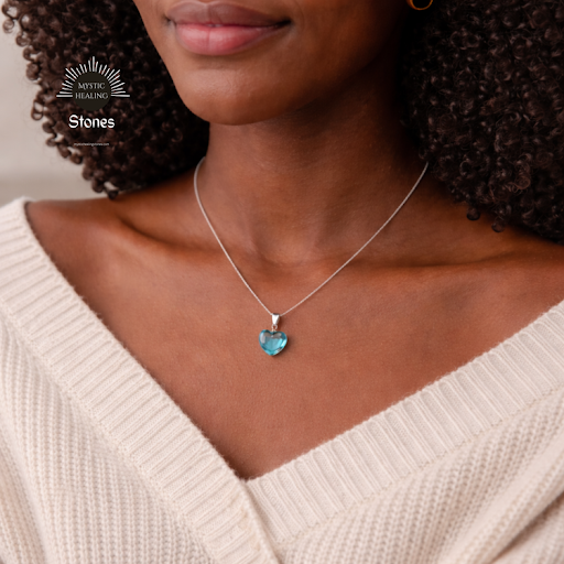 A woman wearing a silver chain necklace with an aquamarine heart-shaped crystal pendant.