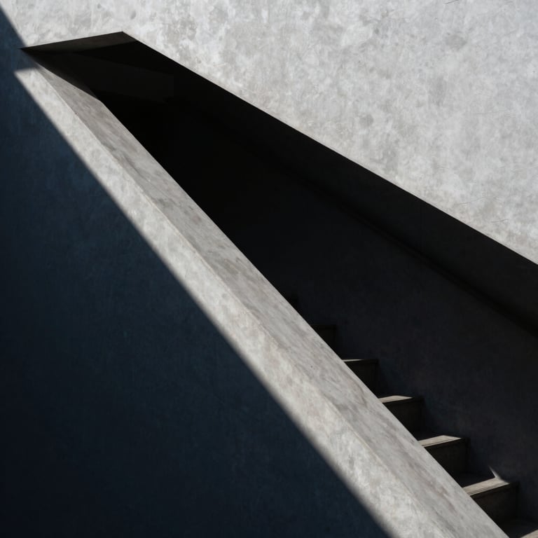 Abstract architectural shot of a modern staircase with sharp geometric shadows and high contrast between light grey and deep navy tones.