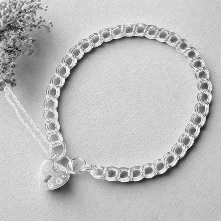 Sterling silver charm bracelet with a heart-shaped padlock clasp on a textured grey background.