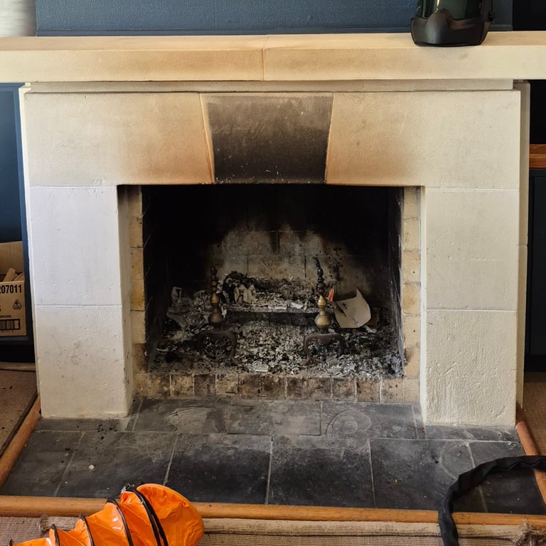 Traditional stone fireplace with soot stains and ashes on a black hearth.