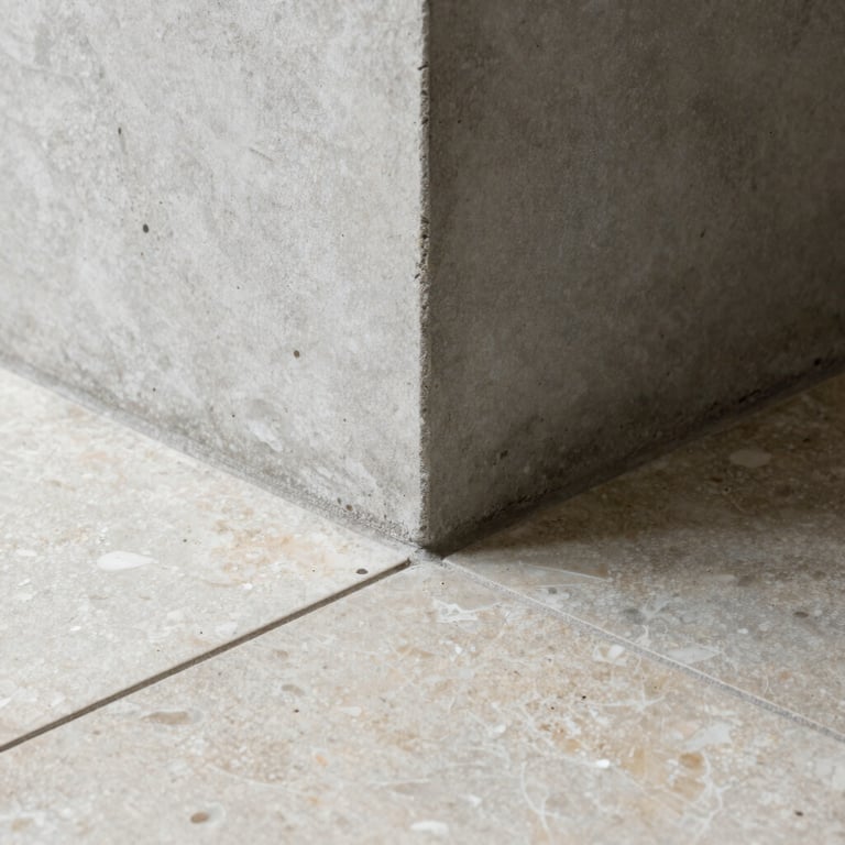 Macro architectural detail showing the clean intersection of a raw concrete column meeting a honed travertine floor tile, soft natural side-light.