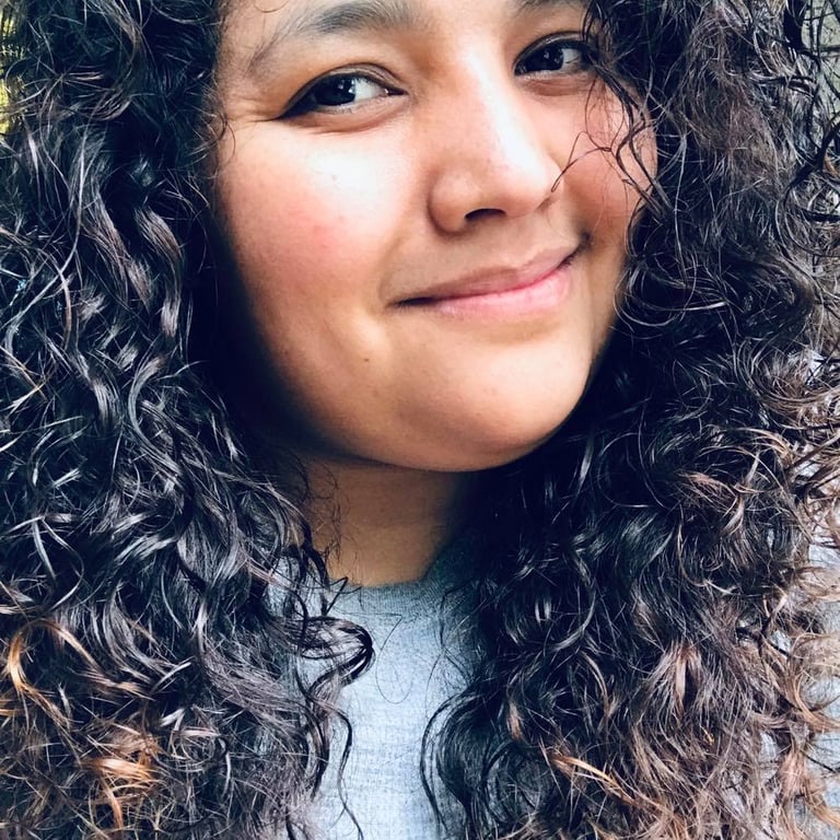 Smiling woman with long dark curly hair and natural makeup in a close-up portrait.